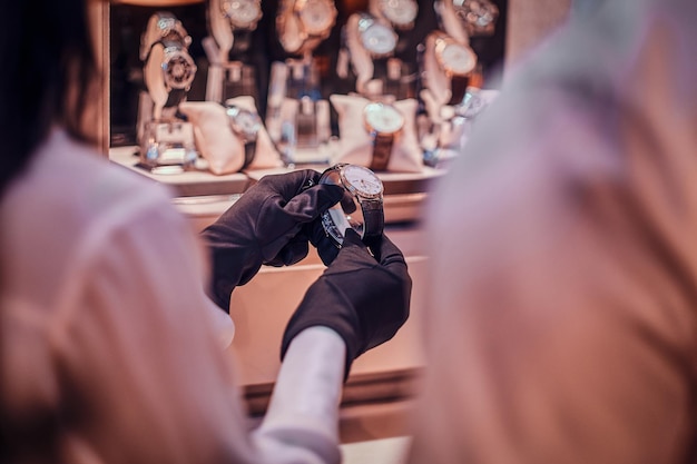 Shop assistant in black gloves is showing expensive watch for a customer.