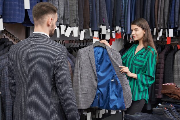 Консультант магазина выбирает и показывает куртку клиенту.