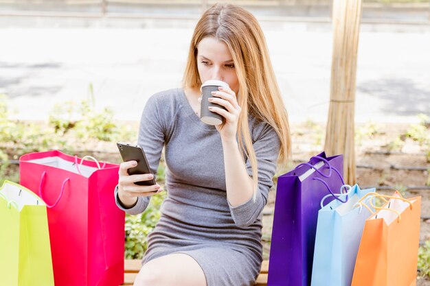Shopaholic woman using cellphone while drinking coffee