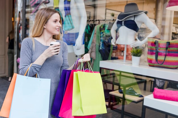 Shopaholic woman with drink looking t window display of a store