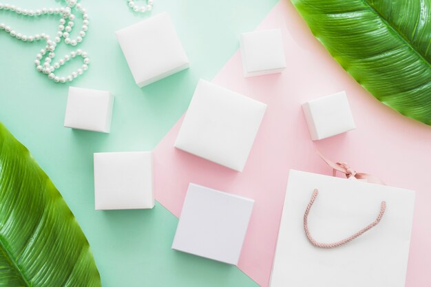 Shopping bag, pearl necklace and different type of white boxes on pastel paper background