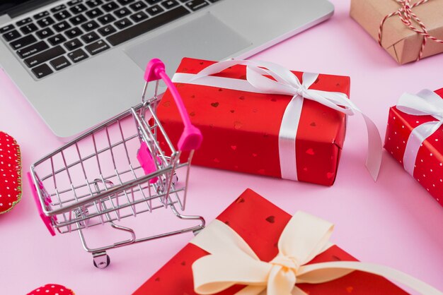 Shopping cart amidst gifts and modern laptop