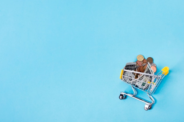 Shopping cart filled with coins on copy space background