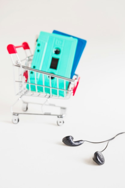 Shopping cart with cassette tapes and black earphone over white background