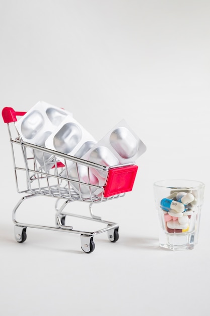 Shopping cart with pill blister and medicines in glass on white background