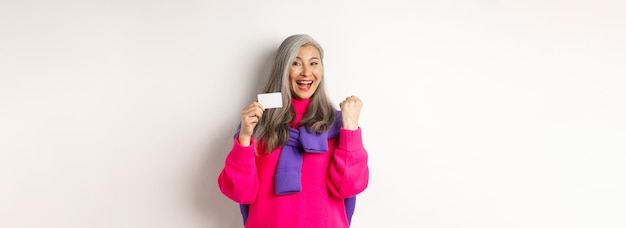 Shopping concept cheerful asian senior woman winning prize from bank showing fist pump gesture and p