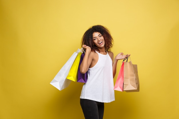 Shopping concept - close up portrait young beautiful attractive african woman smiling and joyful with colorful shopping bag. yellow pastel wall background. copy space.