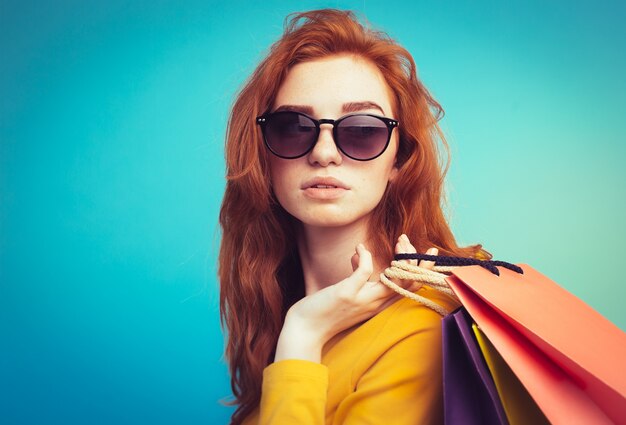 Shopping Concept - Close up Portrait young beautiful attractive redhair girl smiling looking at camera with shopping bag. Blue Pastel Background. Copy space.