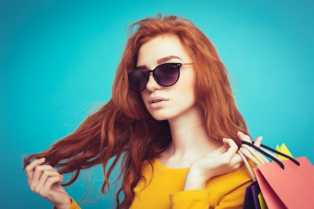 Shopping Concept - Close up Portrait young beautiful attractive redhair girl smiling looking at camera with shopping bag. Blue Pastel Background. Copy space.