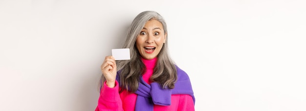 Shopping concept happy asian old aldy looking impressed and showing plastic credit card of her bank