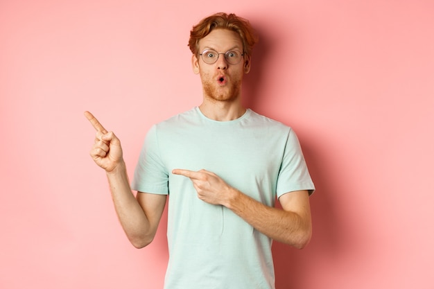 Shopping concept portrait of man with red hair and beard wearing glasses with summer tshirt pointing...