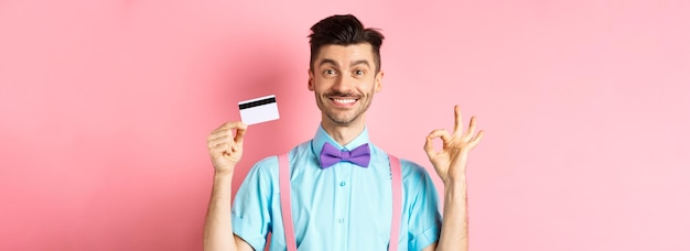 Free photo shopping concept smiling handsome male shopper showing ok sign and plastic credit card buying someth