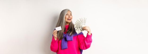 Free photo shopping concept stylish asian senior woman showing money dollars and plastic credit card looking dr