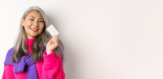 Free photo shopping concept stylish asian senior woman smiling and showing plastic credit card paying contactle