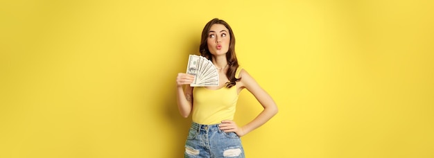 Free photo shopping credit and money concept young brunette woman showing cash and smiling pleased standing ove