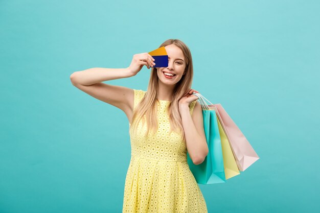 쇼핑 및 라이프스타일 개념: 신용 카드와 다채로운 쇼핑백을 든 아름다운 어린 소녀. 파란색 배경에 고립.