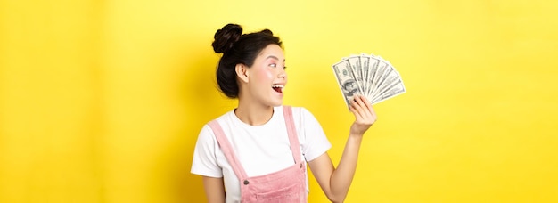 무료 사진 행복 한 얼굴로 달러 지폐를 보고 돈을 보여주는 풍부 하 고 세련 된 아시아 여성 모델 쇼핑