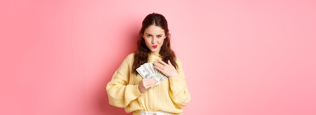 Free photo shopping sassy young woman smiling and looking confident hugging money holding dollar bills on chest