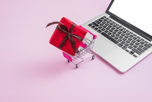 Shopping trolley and gift near modern laptop