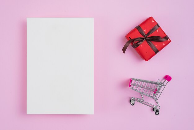 Shopping trolley and gift near paper sheet