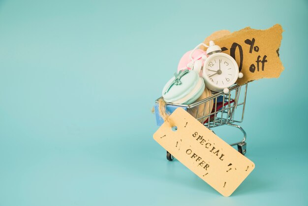 Shopping trolley with alarm clock, bits of paper and macaroons near sale tag