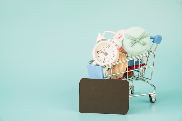 Shopping trolley with alarm clock and macaroons near black tag