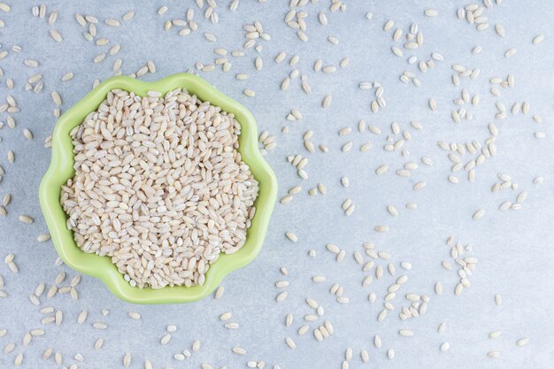 Short-grain rice scattered about and filled into a green bowl on marble background.