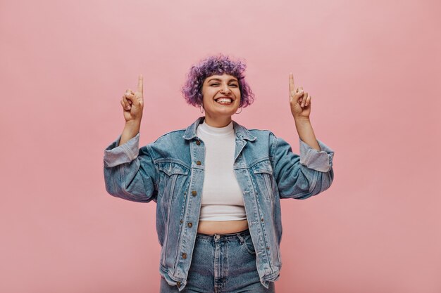 Short-haired curly woman in fashionable clothes smiles. Pretty woman with lilac hair having fun.