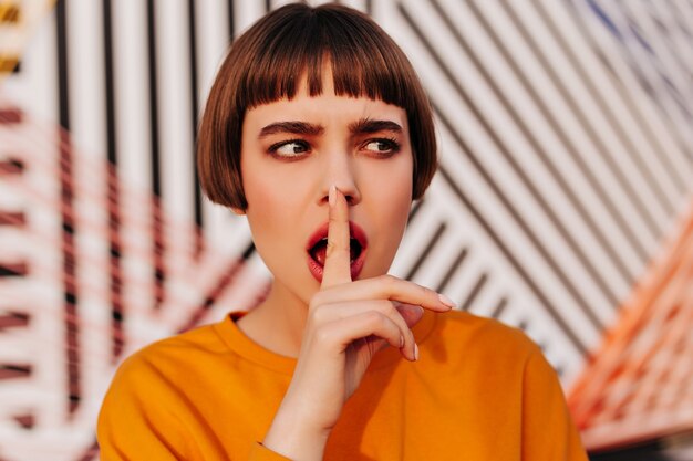 Short-haired lady in orange modern sweatshirt looking away outside