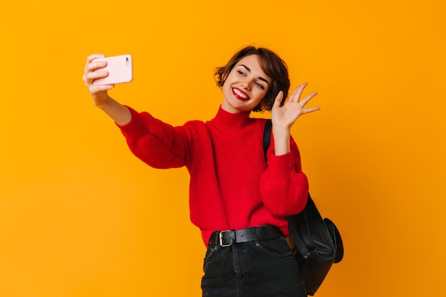 Short-haired white woman waving hand on yellow wall