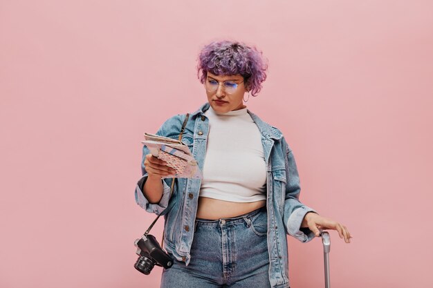 Short-haired woman in white short top carefully read the map. Wonderful curly woman in denim jacket with camera posing.