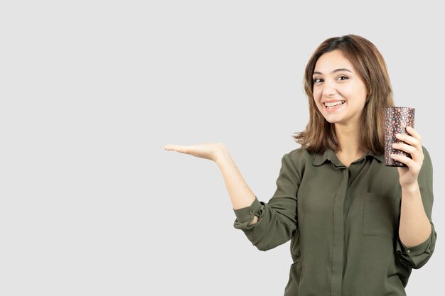 Short-haired young girl holding cup of latte over white wall. High quality photo