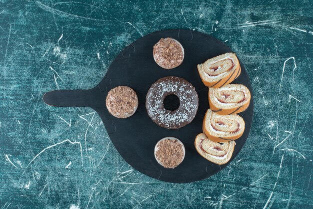 Shortbreads, donut and sliced roll cake on the cutting board , on the blue table. 