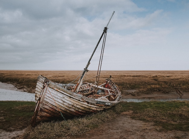 Shot of an abandoned broken boat left by the riverbank surrounded by a wheat field