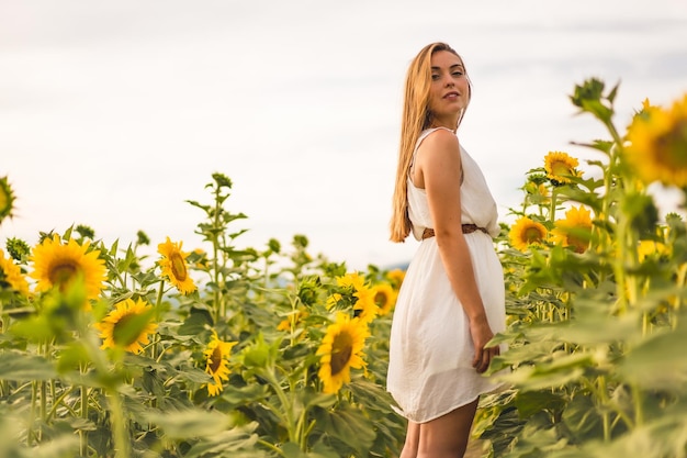 Scatto di un'attraente donna bionda con un vestito bianco in posa in un campo di girasoli