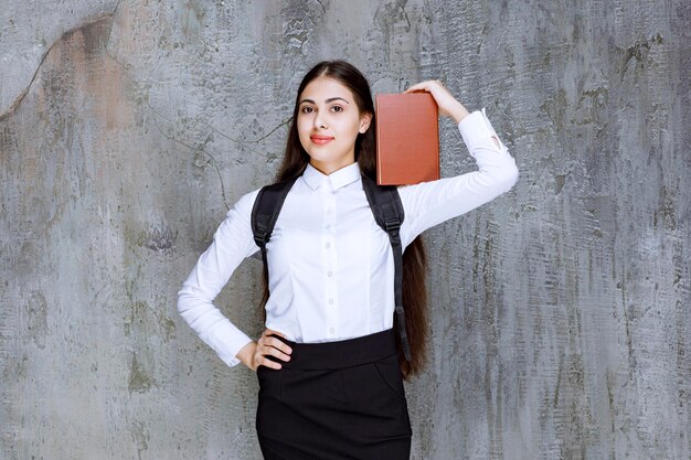 Shot of beautiful teenager with backpack showing book to camera. High quality photo