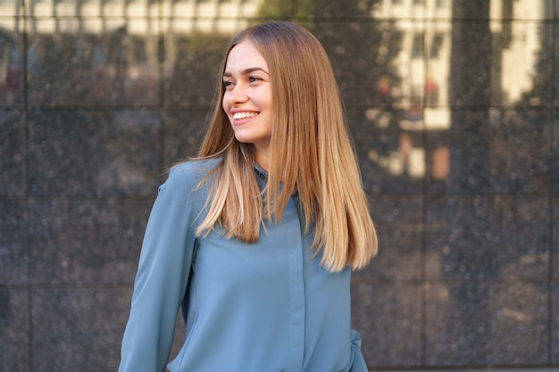 Shot of beautiful young businesswoman wearing blue chiffon shirt while standing and posing on gray marble wall