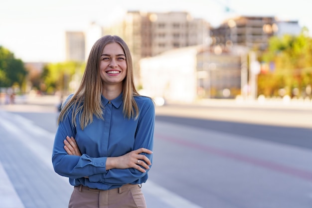 Shot of beautiful young businesswoman wearing blue chifon shirt while standing on the street with folded arms.