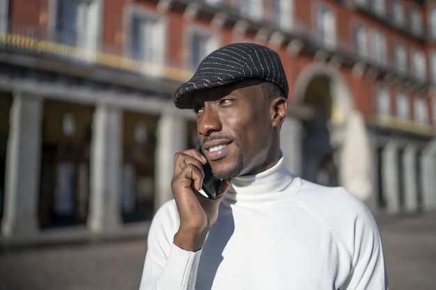 shot of a black man wearing a hat and a turtleneck talking on phone