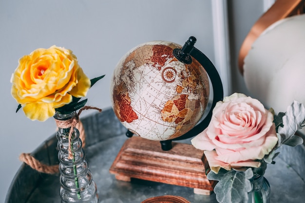 Free photo shot of a brown world globe beside yellow and pink roses in vases