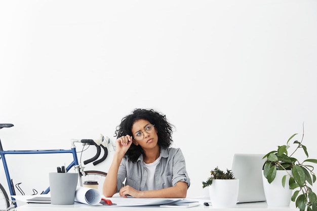 Shot of cute young entrepreneur with dark curly hair wearing shirt and round eyeglasses