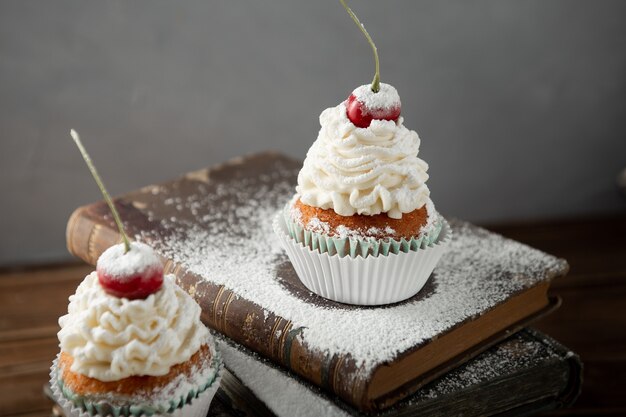 Shot of delicious cupcakes with cream, powdered sugar, and a cherry on top on books