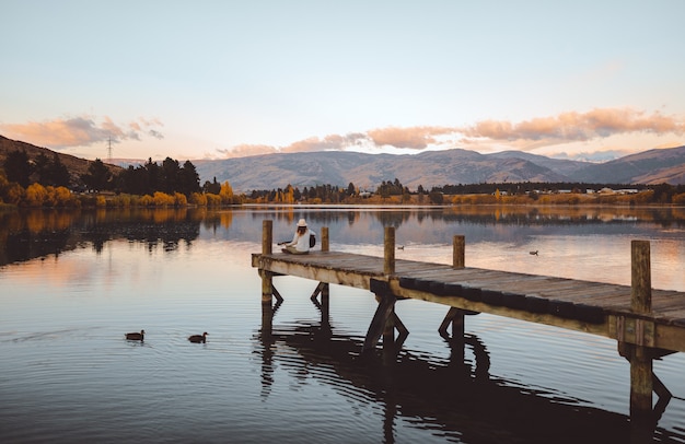 Free photo shot of a female sitting on the pier playing the guitar in cromwell, new zealand