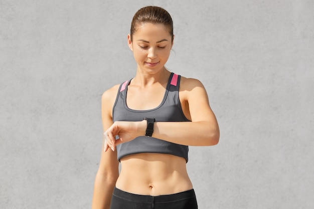 Shot of fitness lady or jogger looks attentively at smart watch, checks pulse and counts calories, has healthy lifestyle