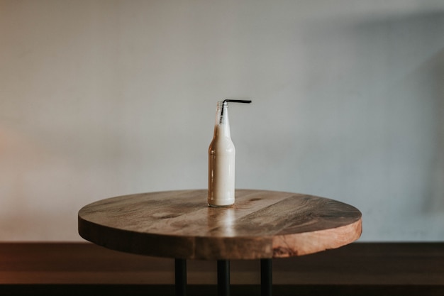 Free photo shot of a glass bottle with a black straw filled with a beverage on a brown wooden table