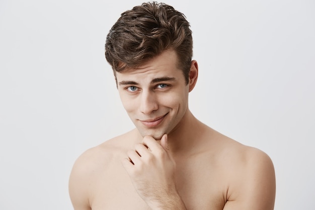 Shot of handsome attractive young caucasian male expressing positive emotions as has good mood after walk with girlfriend. Pleasant looking guy smiles  holding hand under his chin.