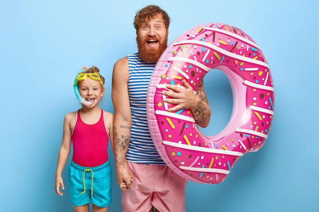 Shot of happy ginger father and daughter posing in pool outfits