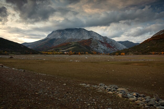 Shot of land with sand on the front with rocky mountains with slight snow