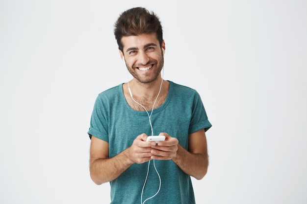 shot of looking happy young man broadly smiling as he talks to his girlfriend during online call using earphones and his electronic gadget. People, technology and communication concept