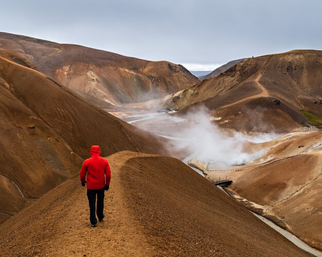 アイスランド、ハイランド地方の丘を歩いている赤いコートを着た男の後ろのショット